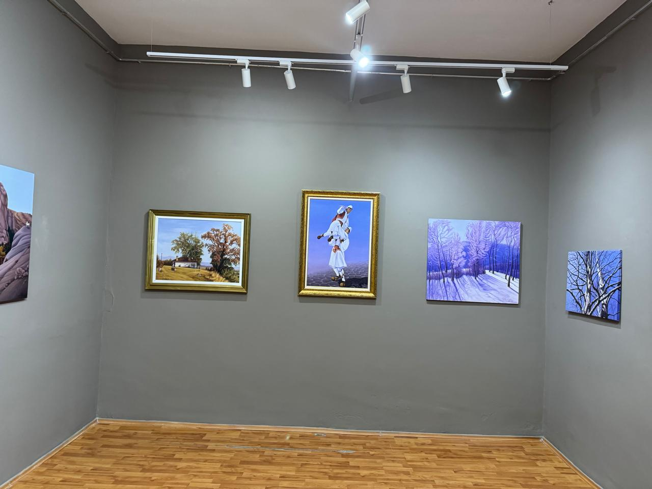 A rural landscape, a figure in traditional dress, and winter woodland paintings displayed together in a gallery.